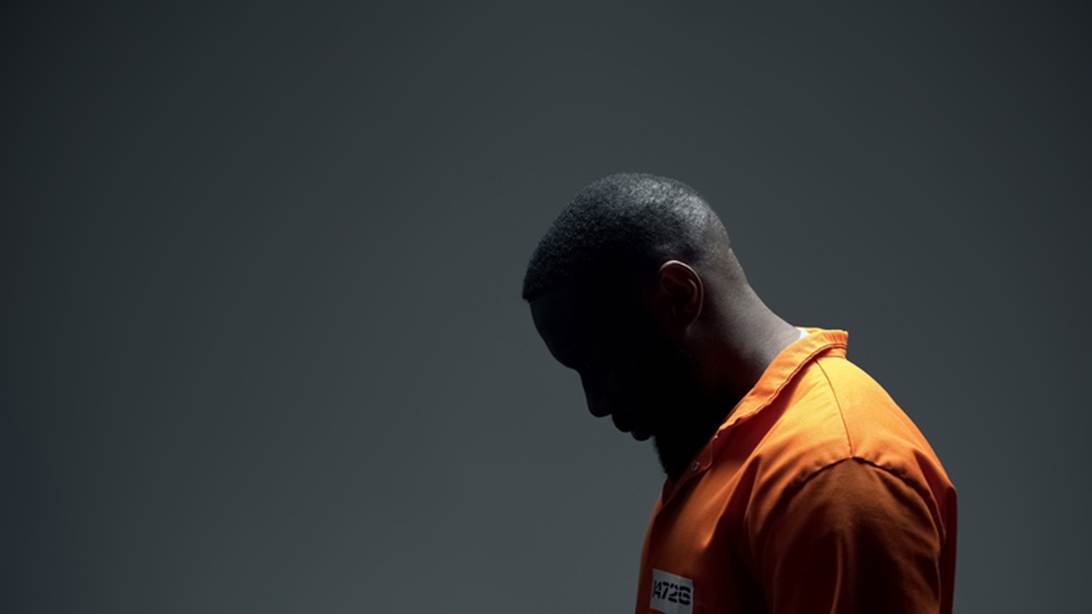 A somber photo shows a Black man in an orange jumpsuit. He is looking down, in shadow, with the text "4726" on his chest.